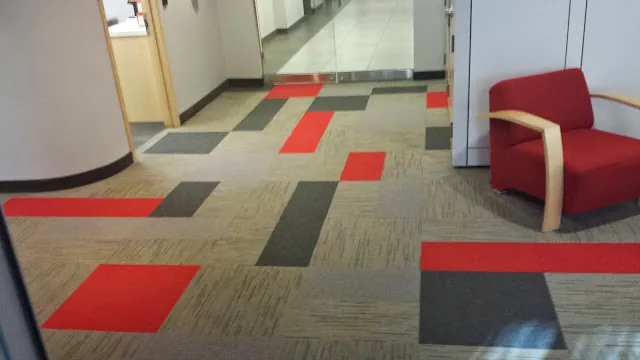 Custom red and gray modular carpet tile installation with a matching red lounge chair by Geometrix Flooring & Design