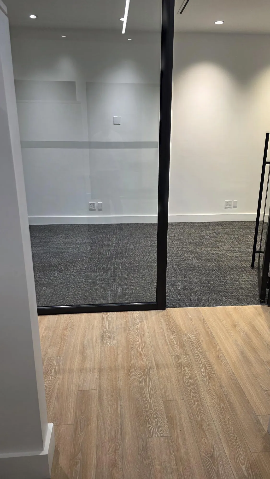 Glass-partition commercial office with gray carpet tile inside and wood-look luxury vinyl plank in the corridor, installed by Geometrix Flooring & Design